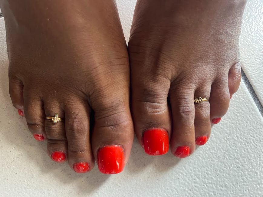 Pédicure vernis rouge corail brillant avec bagues d'orteil dorées